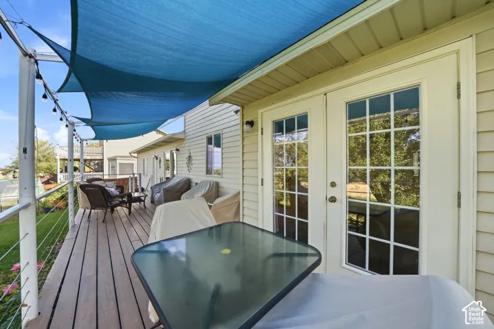 Exterior deck featuring wood-finish decking, horizontal cable railing, overhead shade sails, and double-pane glass French doors