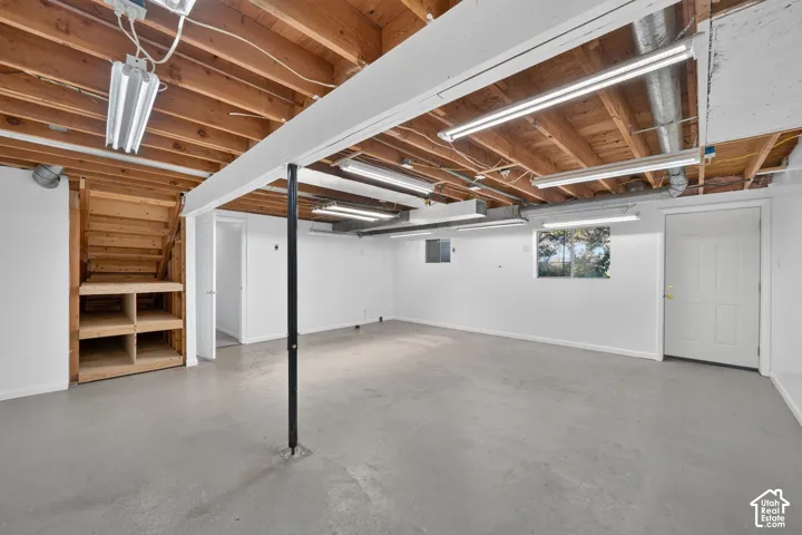 Open-concept unfinished space featuring exposed wood joist ceilings, painted concrete flooring, built-in wooden shelving, and linear LED lighting