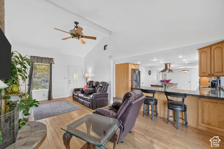 Vaulted ceilings, wood-finish flooring, stone-surround fireplace, and kitchen featuring cabinetry with an integrated breakfast bar