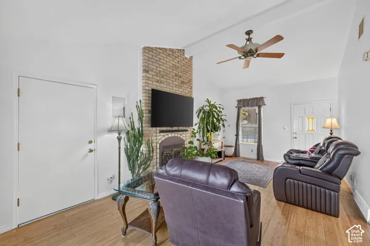 Living area featuring a vaulted ceiling, wood-finish flooring, full-height masonry fireplace, and a ceiling fan