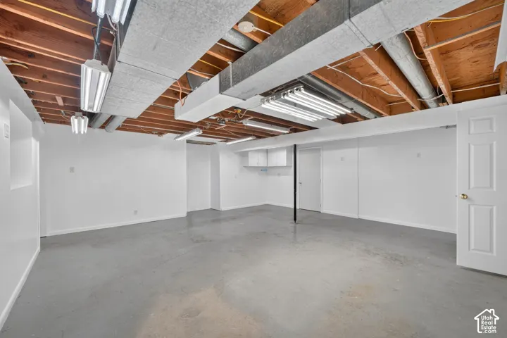 Open-concept room featuring exposed wood joist ceilings, painted concrete flooring, wall-mounted fluorescent lighting fixtures, and white-painted walls