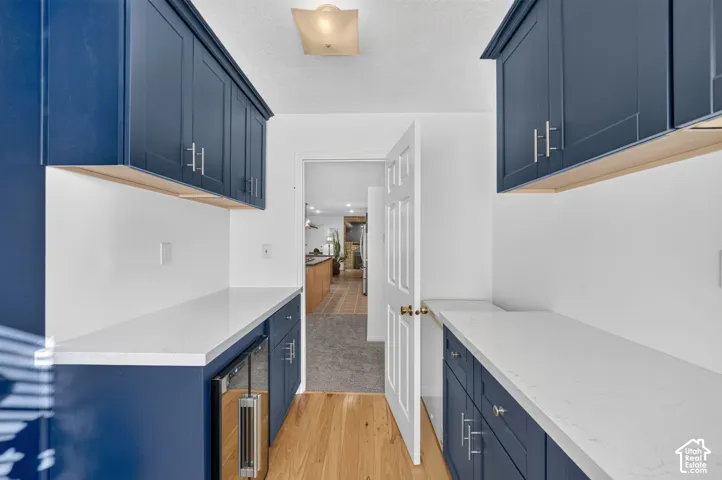 Navy cabinetry with stainless steel hardware, white stone-composite countertops, built-in beverage refrigerator, and wood-finish flooring