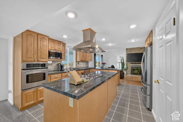 Kitchen featuring a central island with a gas cooktop and stainless steel range hood, stone countertops, wood cabinetry, built-in stainless steel wall oven, and tile flooring