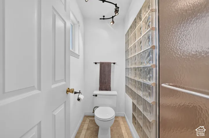 Bathroom featuring a glass block wall, tile flooring, track lighting, and a walk-in shower with a textured glass door