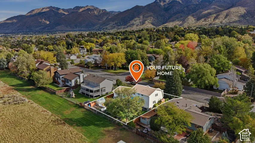 Aerial perspective of a multi-level residence featuring a fenced backyard, mature trees, and a mountain range backdrop