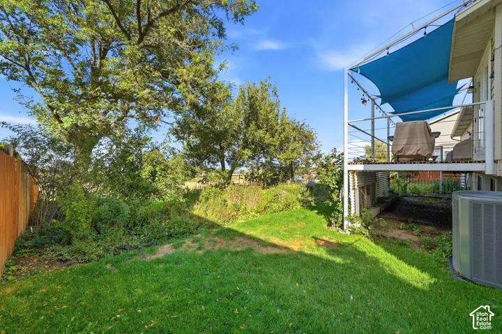 Private backyard featuring a manicured lawn, mature trees, wood privacy fencing, and an elevated deck with a metal support structure