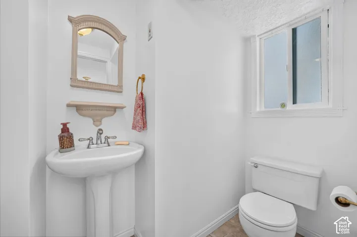 White pedestal sink with a metallic faucet, wall-mounted arched mirror with integrated shelf, window with white trim, and a standard toilet