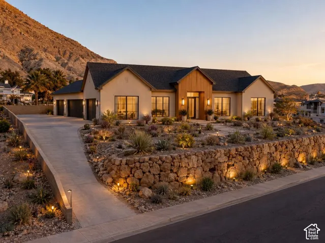 Single-story exterior featuring light-toned stucco, wood-paneled entryway, multi-car garage, terraced natural stone retaining wall, and desert-inspired xeriscaping