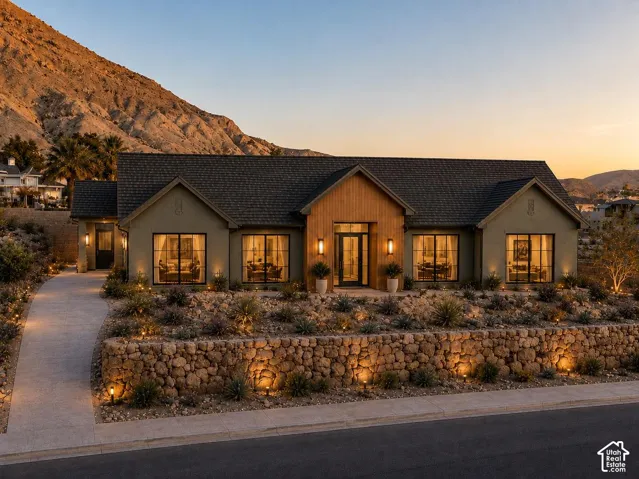 Single-story residence featuring stucco exterior, vertical wood siding accents, large grid-pattern windows, a stacked stone retaining wall, and mountain topography