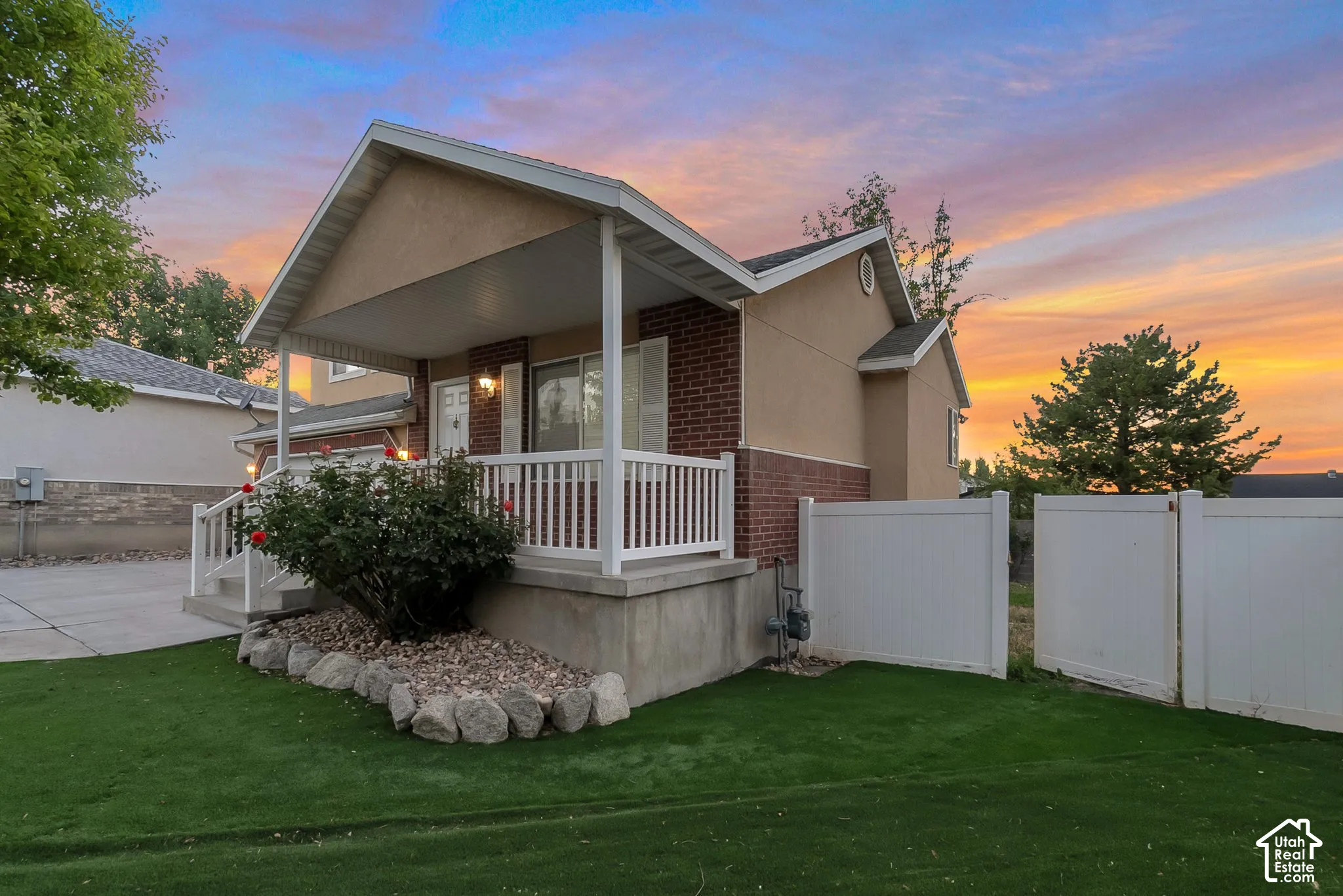 Exterior featuring a brick and stucco facade, a covered front porch with white railing, and a fenced yard with landscape rock edging