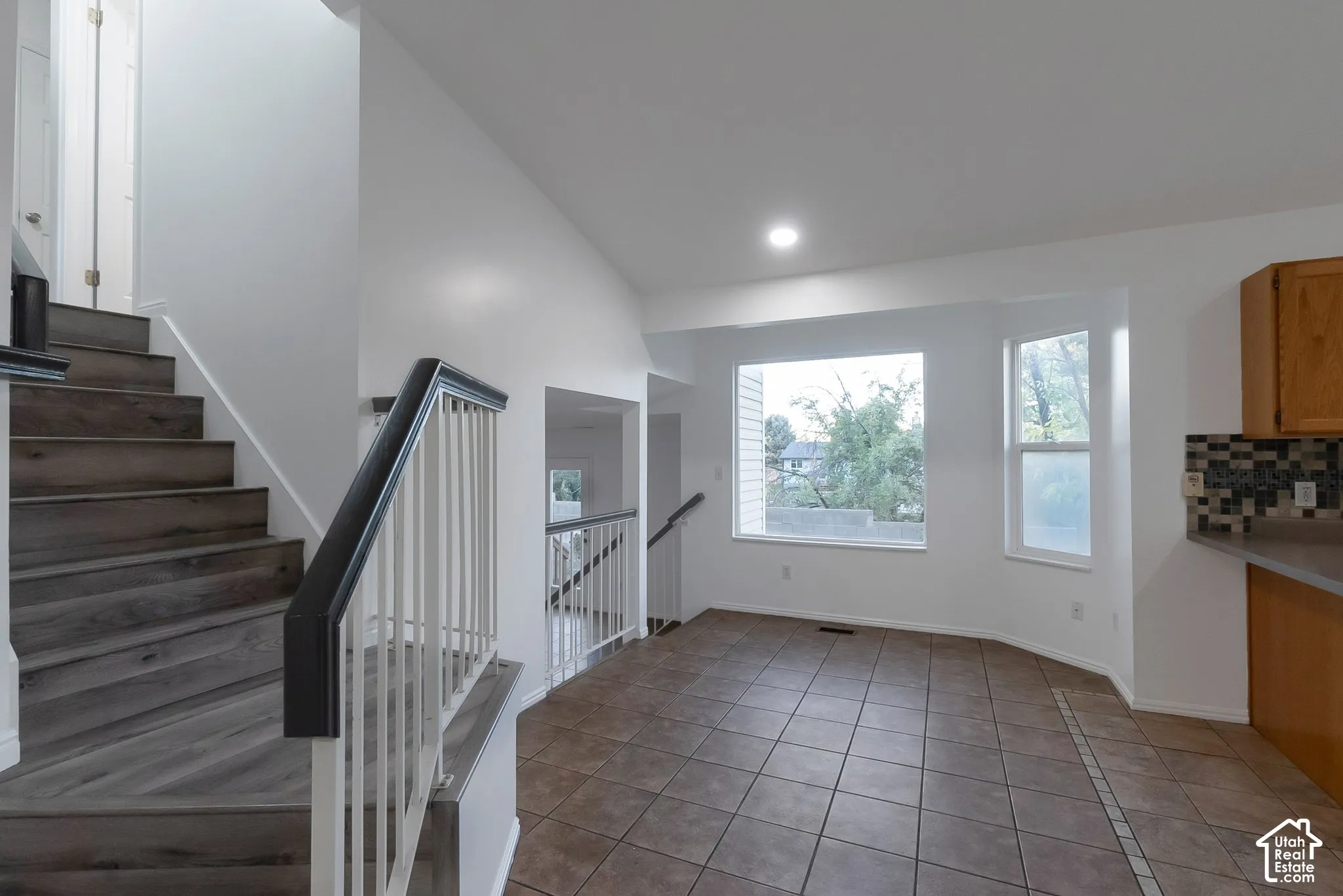 Staircase featuring wood-finish treads and white metal railings, tile flooring, vaulted ceilings, and multi-pane windows