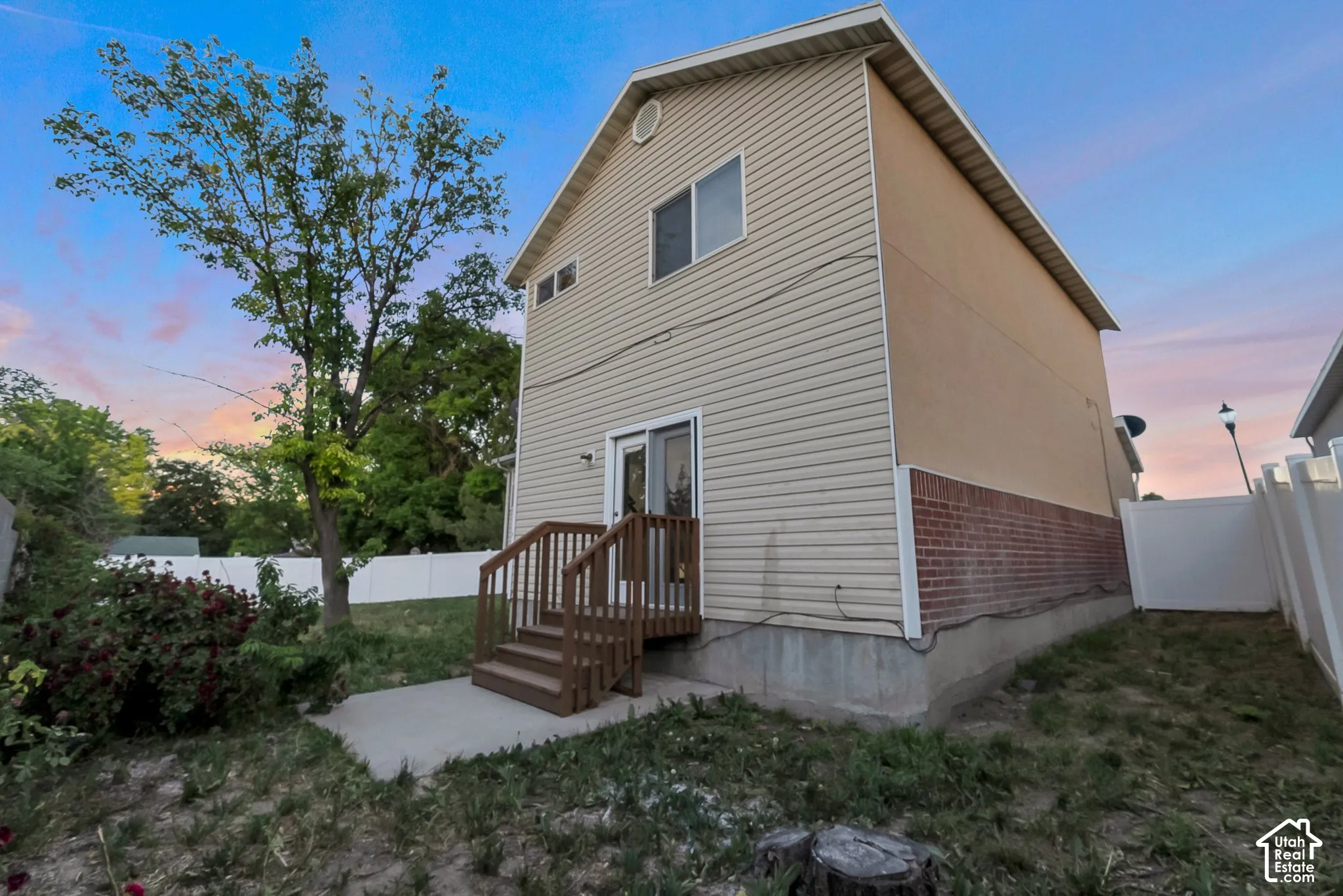 Two-story exterior featuring light-colored horizontal siding, a red brick base, a rear wood-framed staircase, and a concrete patio