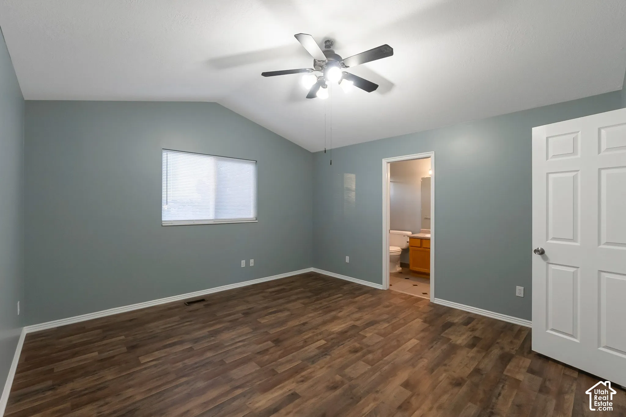 Vaulted ceiling with a central multi-light fan, wood-finish flooring, and a six-panel interior door