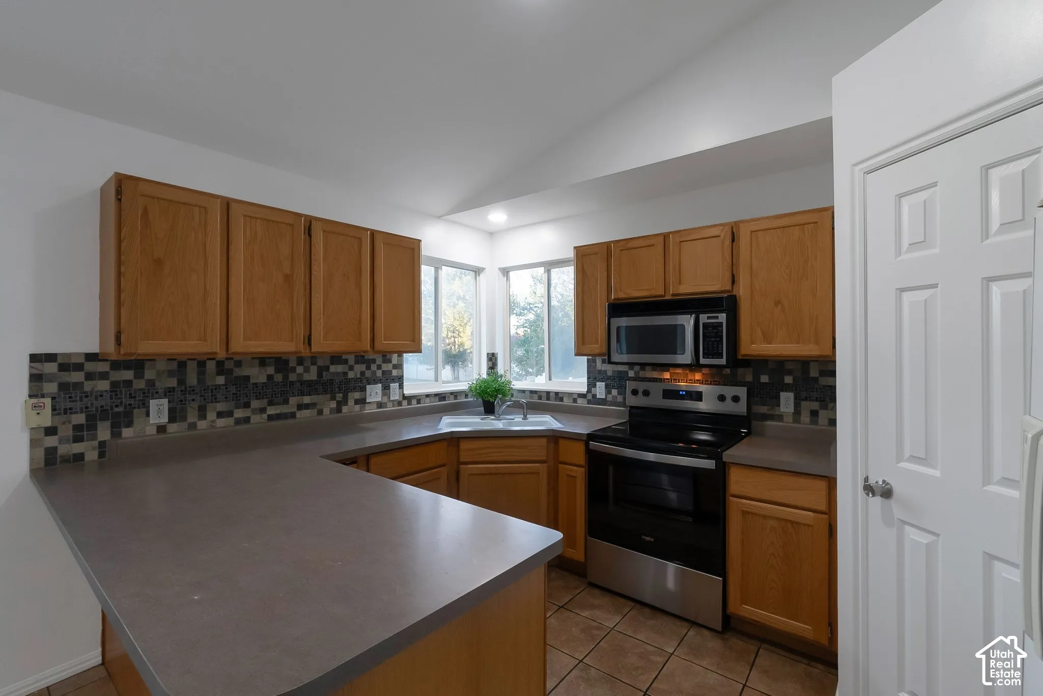 Kitchen featuring wood cabinetry, solid surface countertops, multi-toned mosaic tile backsplash, stainless steel range and microwave, and vaulted ceilings