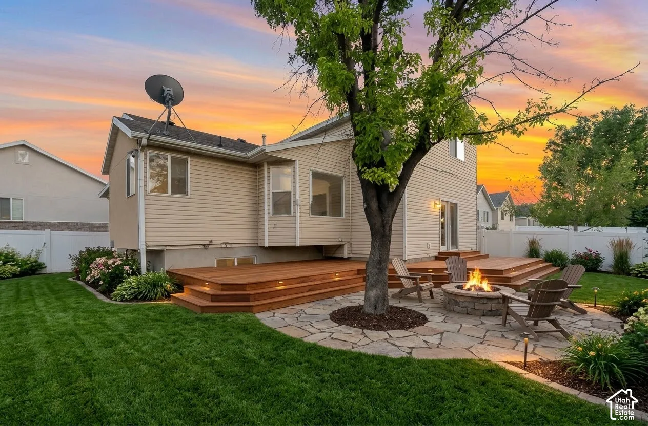 Multi-level wood deck, flagstone patio, built-in stone fire pit, and manicured lawn enclosed by white vinyl fencing