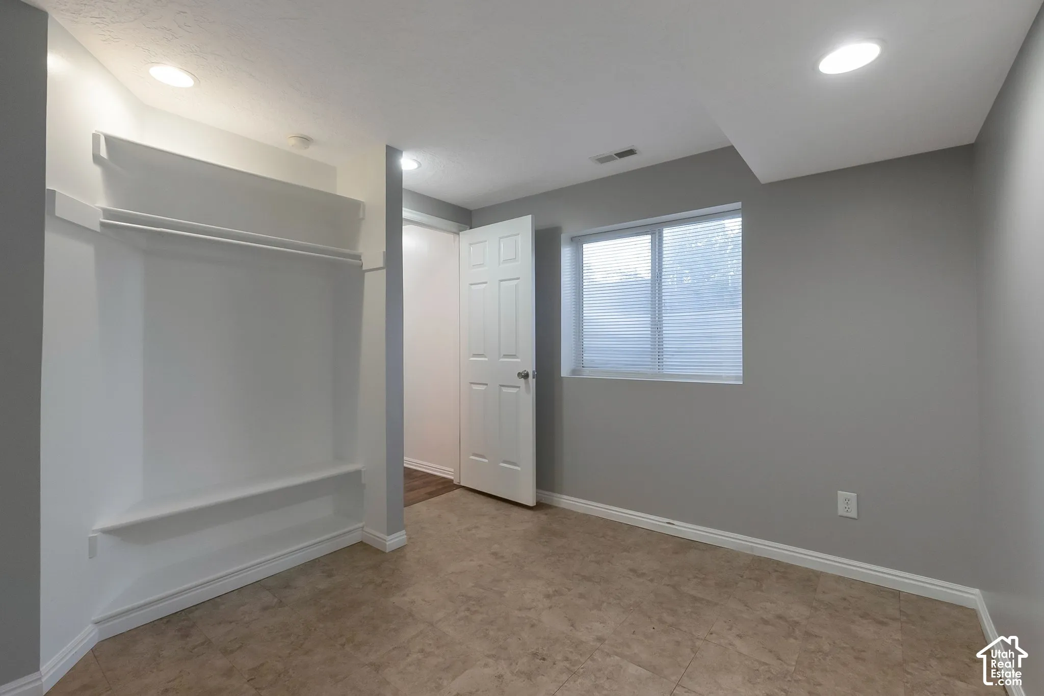 Neutral-toned interior space featuring tile flooring, recessed ceiling lighting, a built-in wall shelf system, and a single-panel door