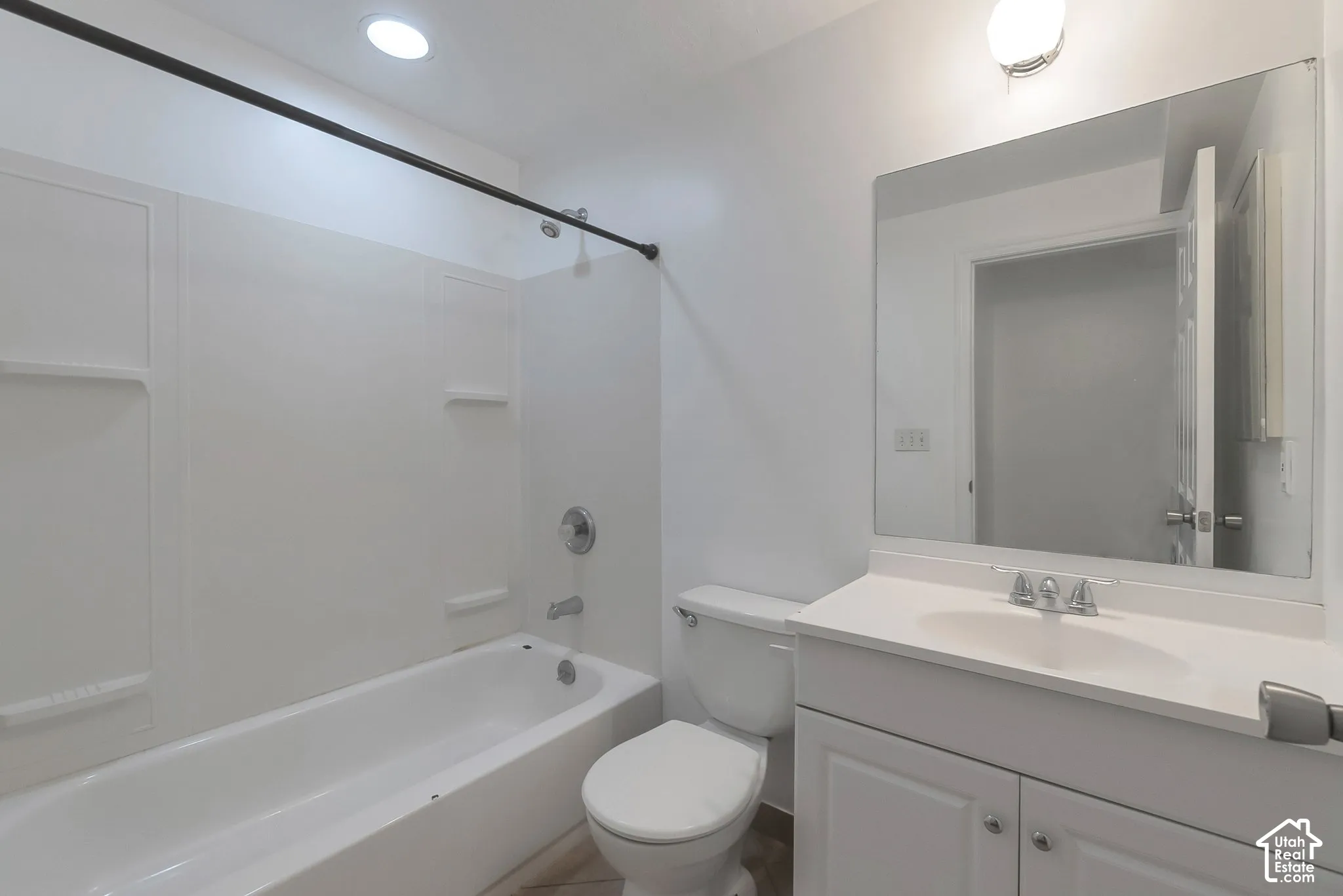 Full-width vanity with an integrated sink, recessed lighting, wall-mounted mirror, and a tub-shower combination with surround