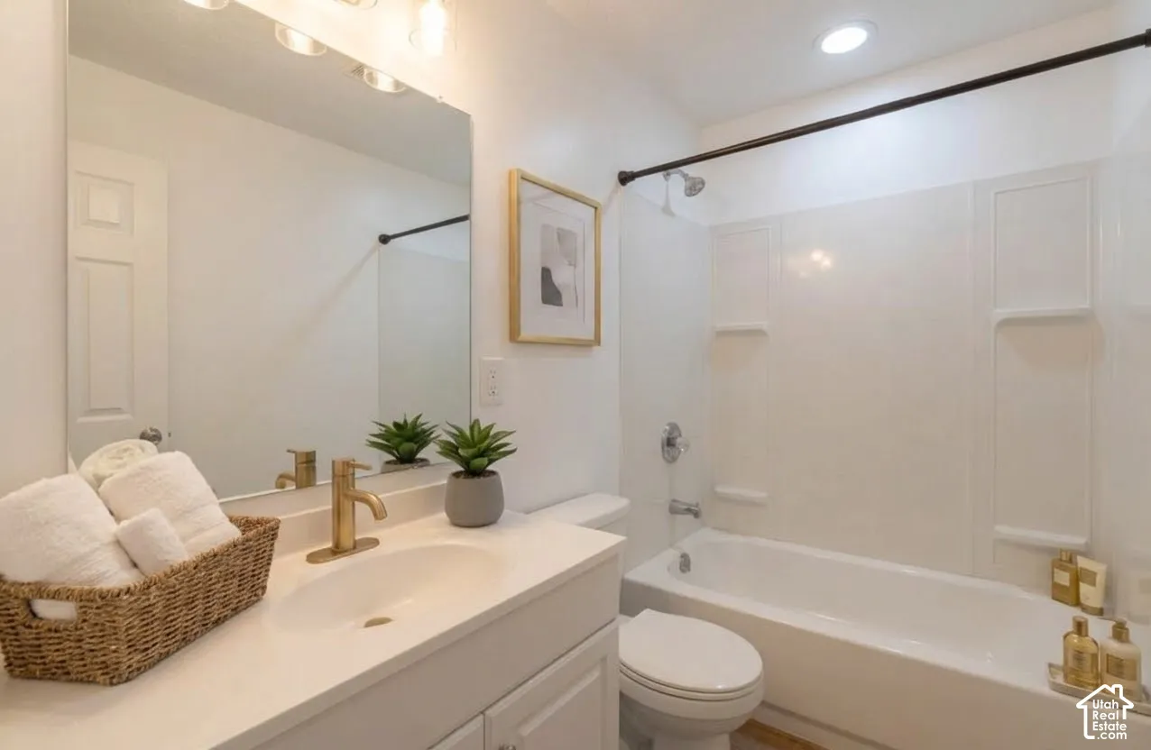 Bathroom featuring a vanity with a solid-surface countertop, brass-finish faucet, full-width mirror, and a shower-tub combination with white surround