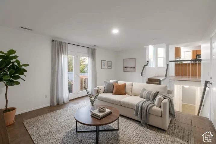 Living area featuring ceramic tile flooring, dual glass-paned doors, recessed ceiling lighting, and staircases with black metal railings