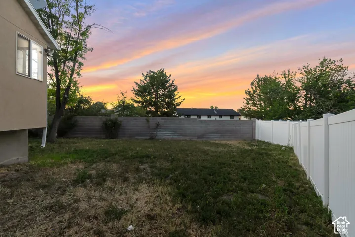 Backyard featuring a white vinyl privacy fence, concrete block perimeter wall, and mature trees