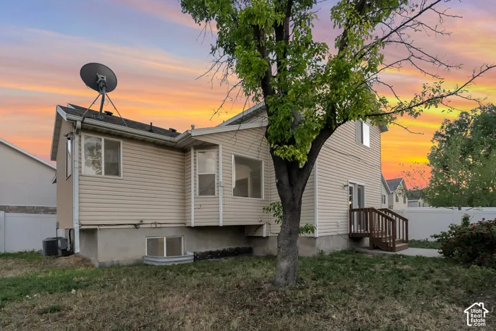 Rear exterior featuring light-toned horizontal siding, a wood deck with stairs, a bay window, and a window well