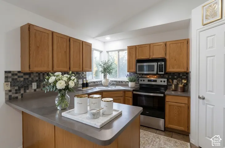 Kitchen featuring wood cabinetry, solid surface countertops, mosaic tile backsplash, stainless steel appliances, and a vaulted ceiling
