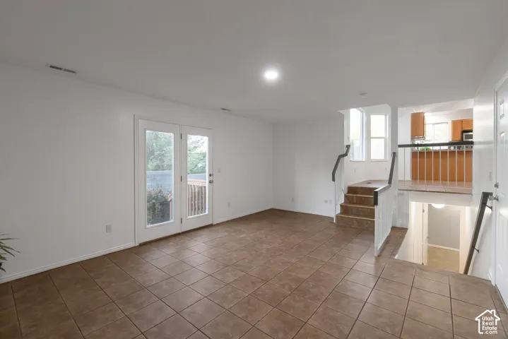 Tile flooring, dual glass-paneled patio doors, recessed ceiling lighting, and a staircase featuring wood-finish steps and a metal railing