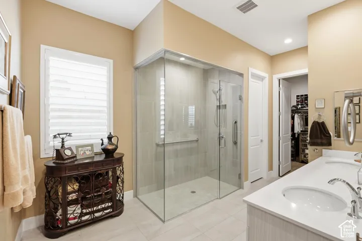 Walk-in glass-enclosed shower with tile surround, double-sink vanity with a solid-surface countertop, and window shutters