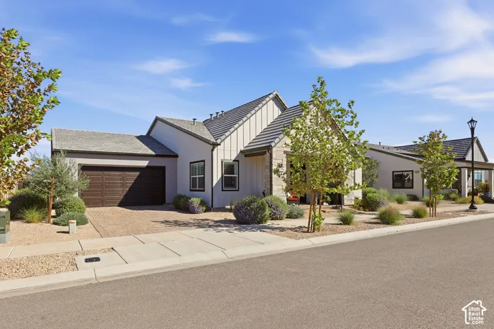 Single-story residence featuring a mixed-material exterior of vertical siding and stone masonry, a pitched tile roof, a double-car garage with paneled doors, and desert-inspired landscaping