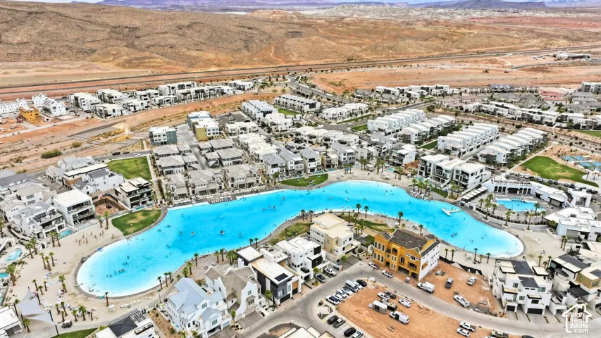 Aerial perspective featuring a large-scale recreational lagoon, landscaped green spaces, palm tree clusters, and desert mountain topography