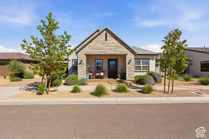 Exterior facade featuring stone veneer masonry, a covered porch, gable roofline, and low-maintenance desert landscaping with mature trees