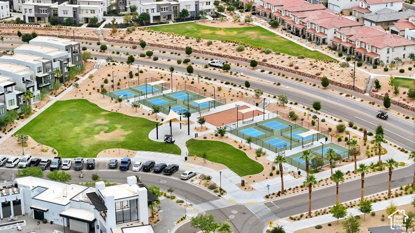 Community recreation area featuring multiple hard-court athletic surfaces, expansive manicured green space, paved pedestrian walkways, and shaded seating structures