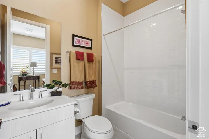 Bathroom featuring a white vanity cabinet with an integrated sink, polished chrome faucet, oversized wall-mounted mirror, and a tub with a white tile surround