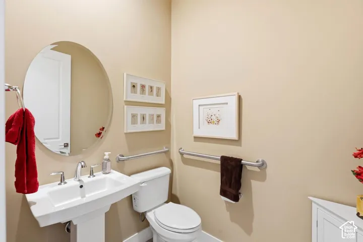 Wall-mounted pedestal sink with widespread faucet, oval frameless mirror, and dual stainless steel grab bars