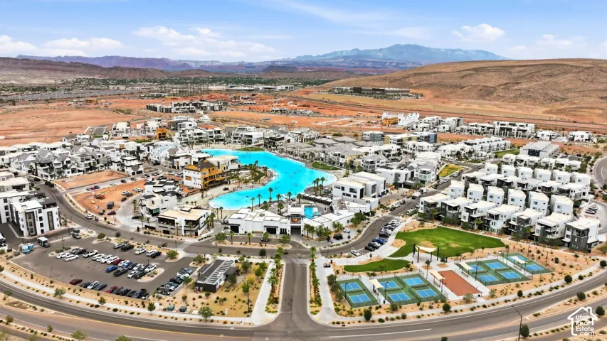 Aerial view featuring a large central swimming lagoon, multi-court tennis facility, manicured green space, paved parking areas, and a desert mountain backdrop