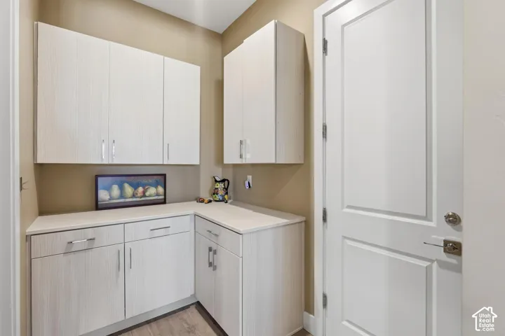 L-shaped configuration of cabinetry featuring light wood-finish slab doors, vertical metal hardware, and solid-surface countertops, accompanied by a white paneled door