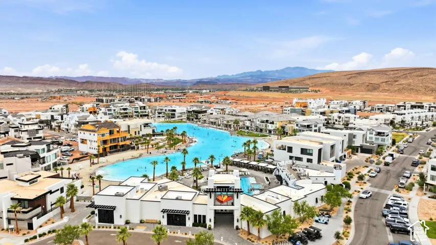 Aerial view featuring a crystalline lagoon, palm tree landscaping, paved streets, and a mountainous backdrop