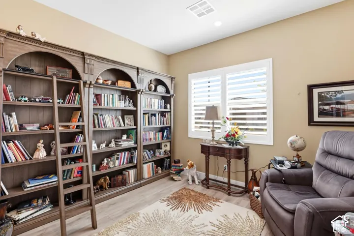 Custom floor-to-ceiling built-in wooden shelving featuring arched architectural detailing and an integrated rolling library ladder, paired with white plantation shutters and wood-finish flooring