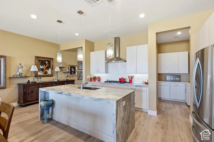 Kitchen featuring a waterfall-edge island with stone-finish countertops, white shaker-style cabinetry, stainless steel range hood, built-in stainless steel refrigerator, and wood-finish flooring