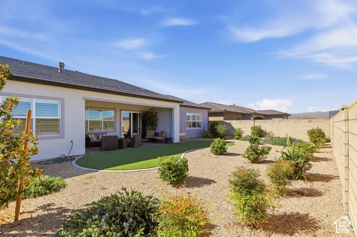 Rear exterior featuring a covered patio, synthetic turf lawn, drought-tolerant landscaping, and concrete block perimeter fencing