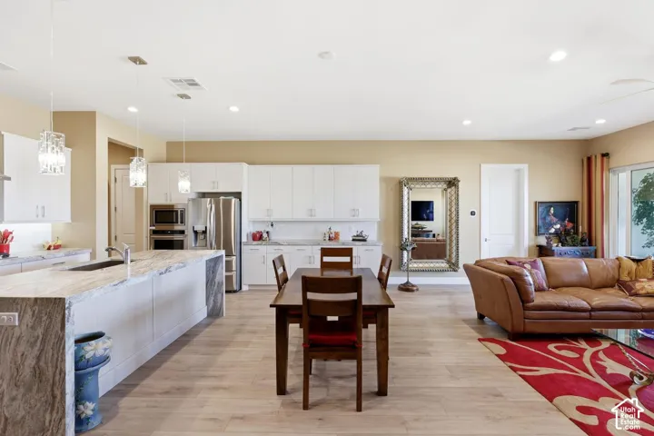 Open-concept kitchen featuring white shaker-style cabinetry, an oversized waterfall-edge island with stone countertop, stainless steel built-in appliances, recessed lighting, and wood-finish flooring