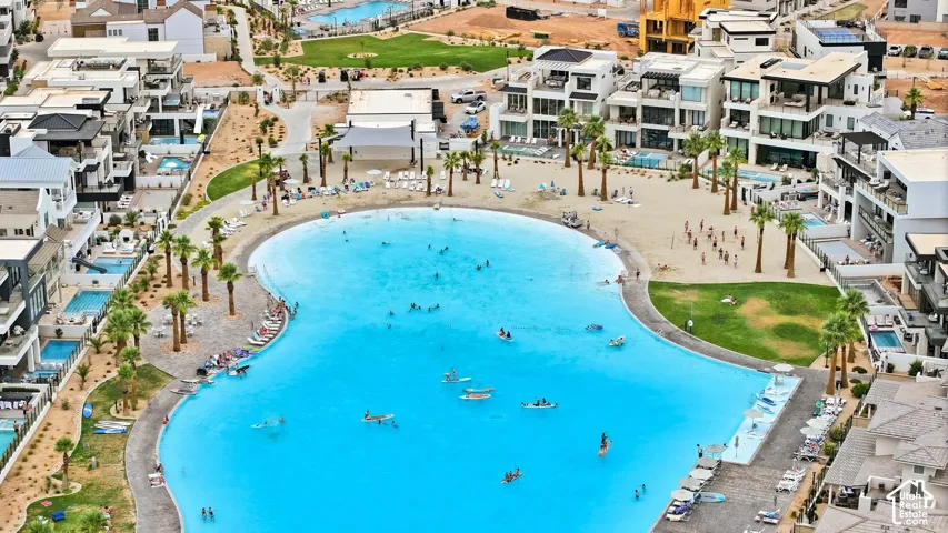 Large-scale aquatic amenity featuring a sandy beach, paved perimeter walkways, palm tree landscaping, and adjacent grass recreation areas