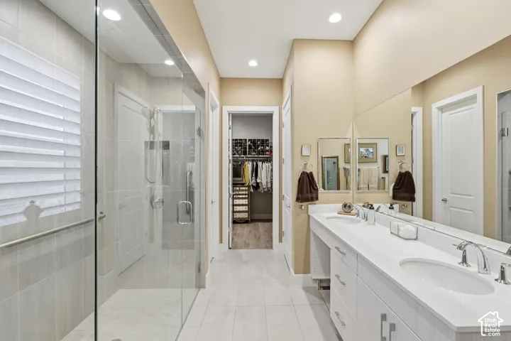 Full-width vanity with dual undermount sinks and quartz countertop, expansive frameless glass walk-in shower with tile surround, large wall-mounted mirror, and recessed lighting