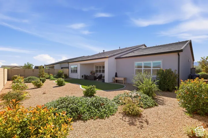 Rear exterior featuring a covered patio, synthetic turf lawn, desert landscaping, and perimeter block wall fencing