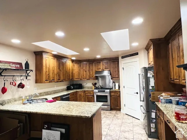 Kitchen featuring custom wood cabinetry, natural stone countertops, dual skylights, recessed lighting, and a stainless steel stove with a matching range hood