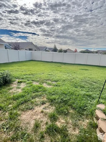 Backyard featuring a grass lawn, perimeter vinyl fencing, and a natural stone retaining wall