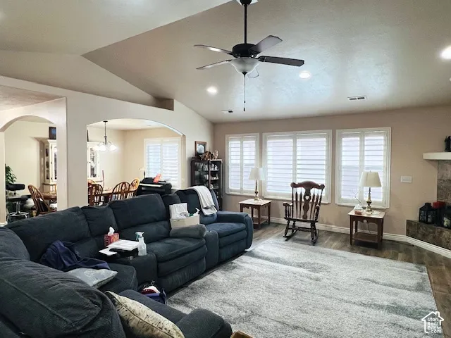Vaulted ceiling featuring a central paddle fan and recessed lighting, wood-finish flooring, plantation shutters, and a stone-surround fireplace