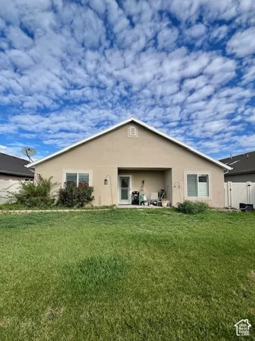 Stucco exterior featuring a covered patio, gabled roofline, dual sliding windows, and a fenced backyard