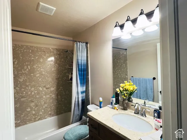 Bathroom featuring a stone-composite countertop with an integrated oval sink, wood-finish vanity cabinetry, four-light vanity fixture, and a tub-shower combination with patterned stone-composite wall surround
