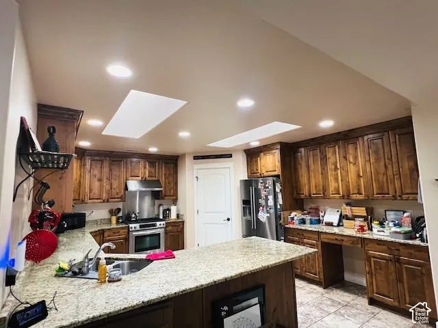 Kitchen featuring stained wood cabinetry, stone-finish countertops, dual skylights, recessed lighting, and a stainless steel slide-in range